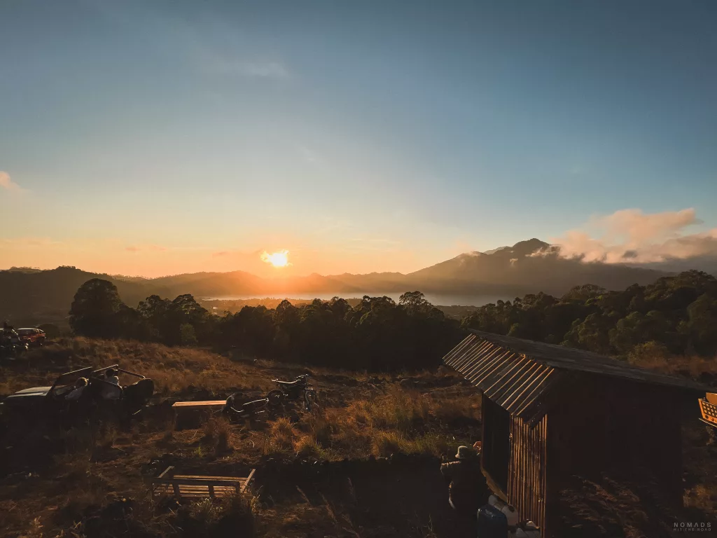 Sonne geht am Mount Batur auf, mit Blick auf den Hang mit Häuschen und Autos