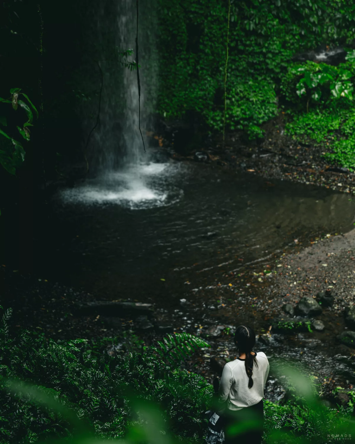 Frau steht am Rand eines Wasserbeckens an einem Wasserfall
