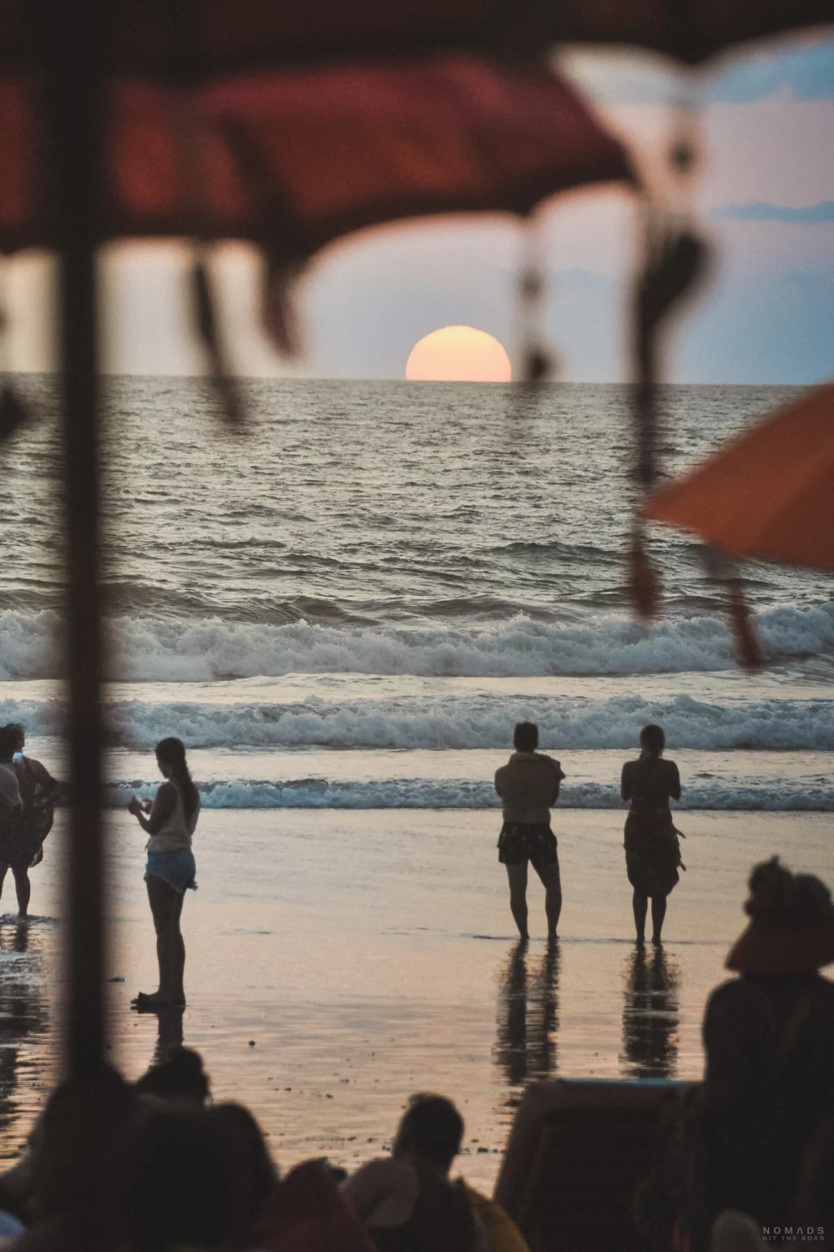 Sonne geht am Horizont über dem Meer unter, während Menschen am Strand sind