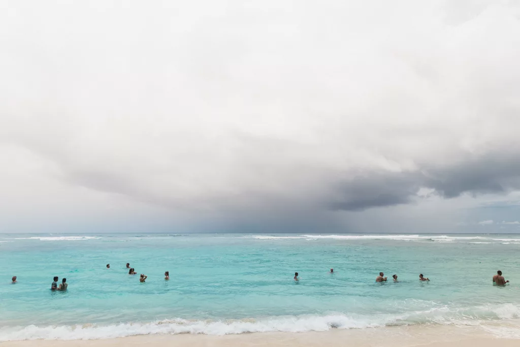 Dunkle Wolken über dem türkisblauen Meer, in dem Menschen baden