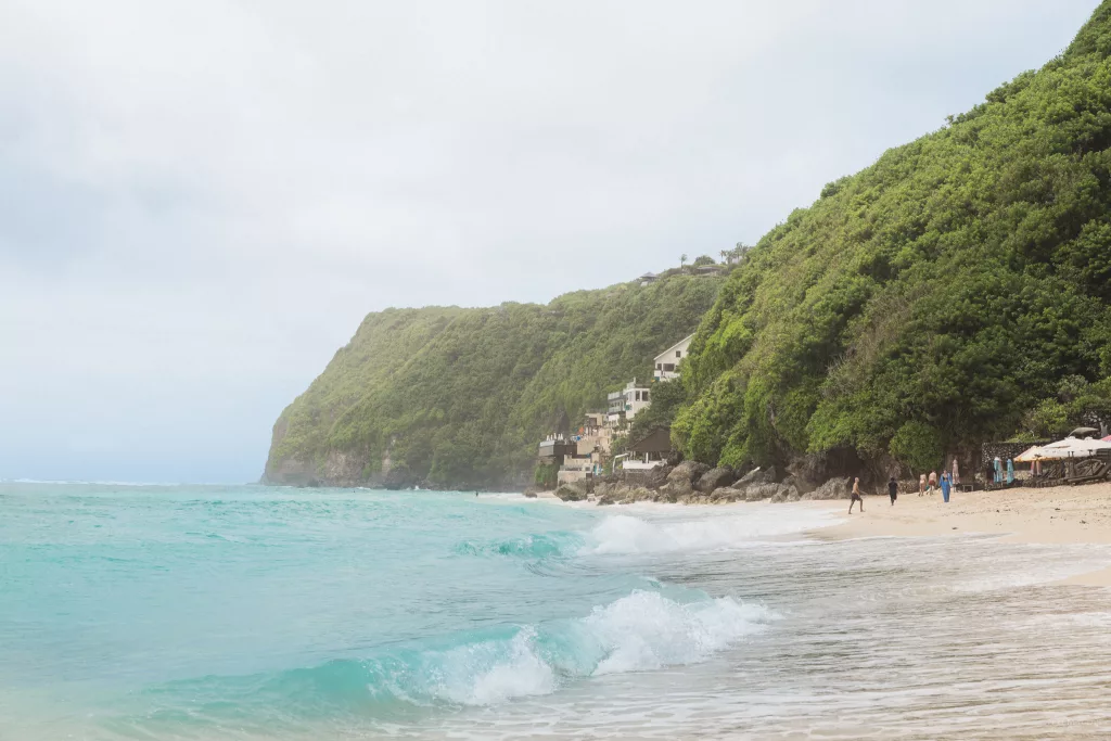 Wellen, die auf den Melasti Beach treffen der umgeben ist von bewachsenen Hängen