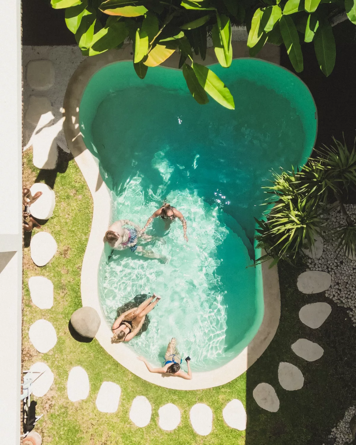 Blick von oben auf einen Pool im Garten, wo Menschen drin sitzen