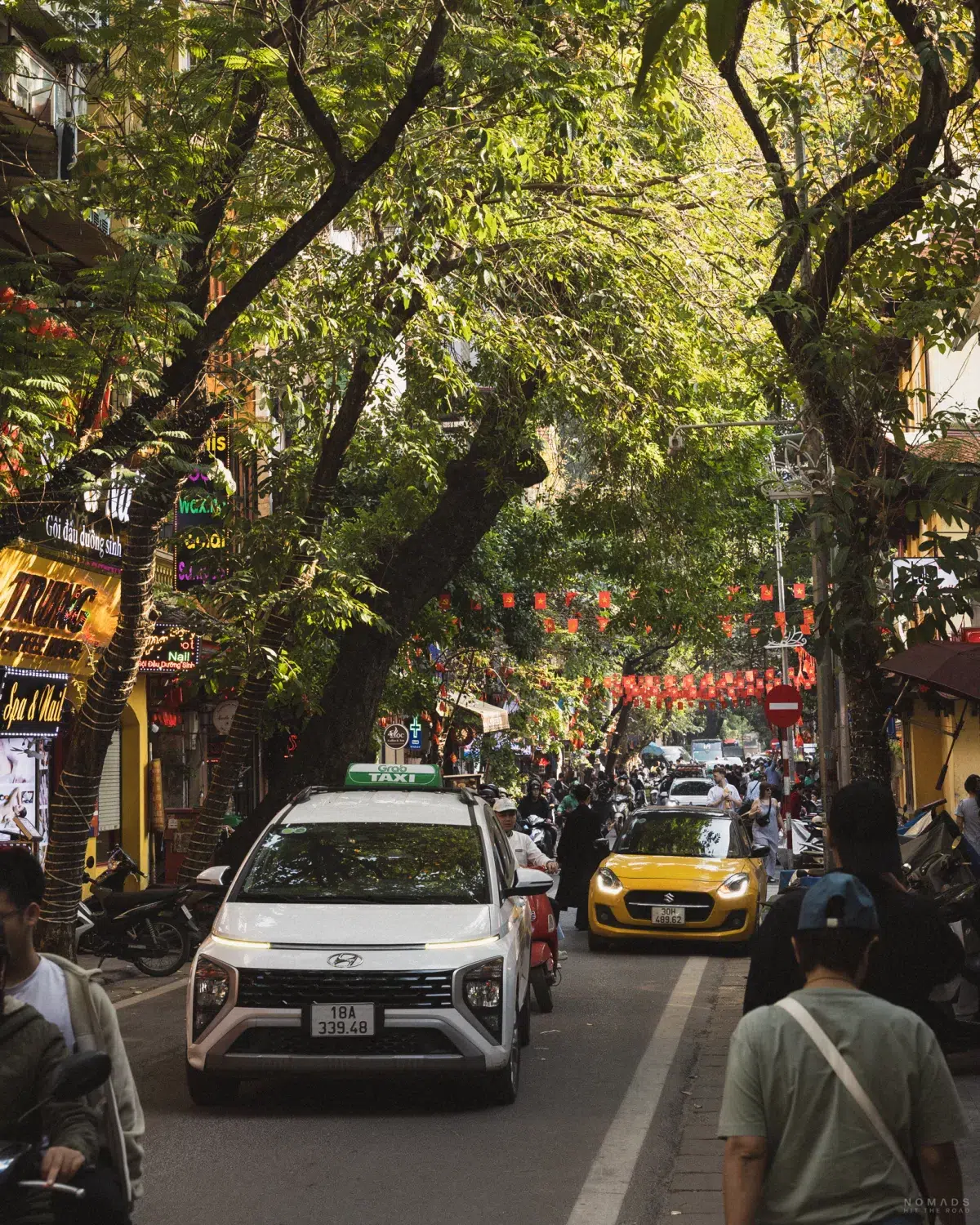 Autos fahren auf einer engen Straße zwischen Häusern und Menschen entlang