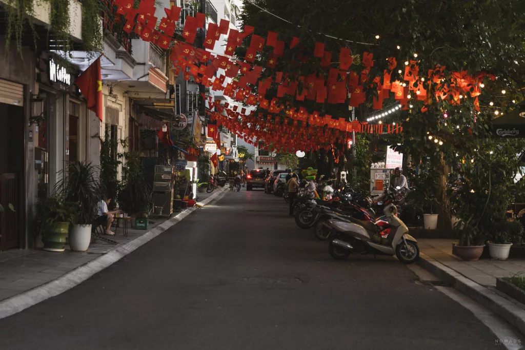 Straße gesäumt mit Wohnhäusern und behangen mit vietnamesischen Flaggen und Moped am Straßenrand
