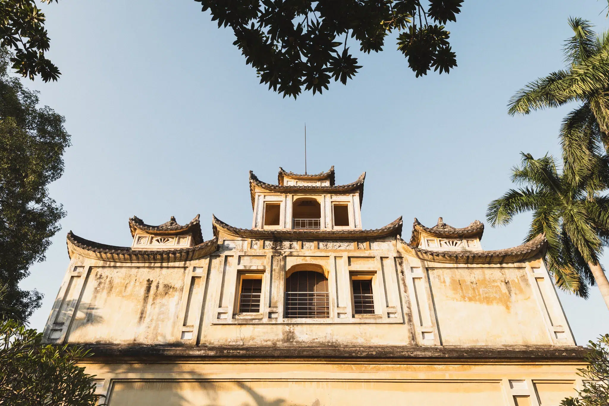 Blick auf ein Gebäude umgeben von Palmen und Bäumen auf dem Gelände der Zitadelle in Hanoi