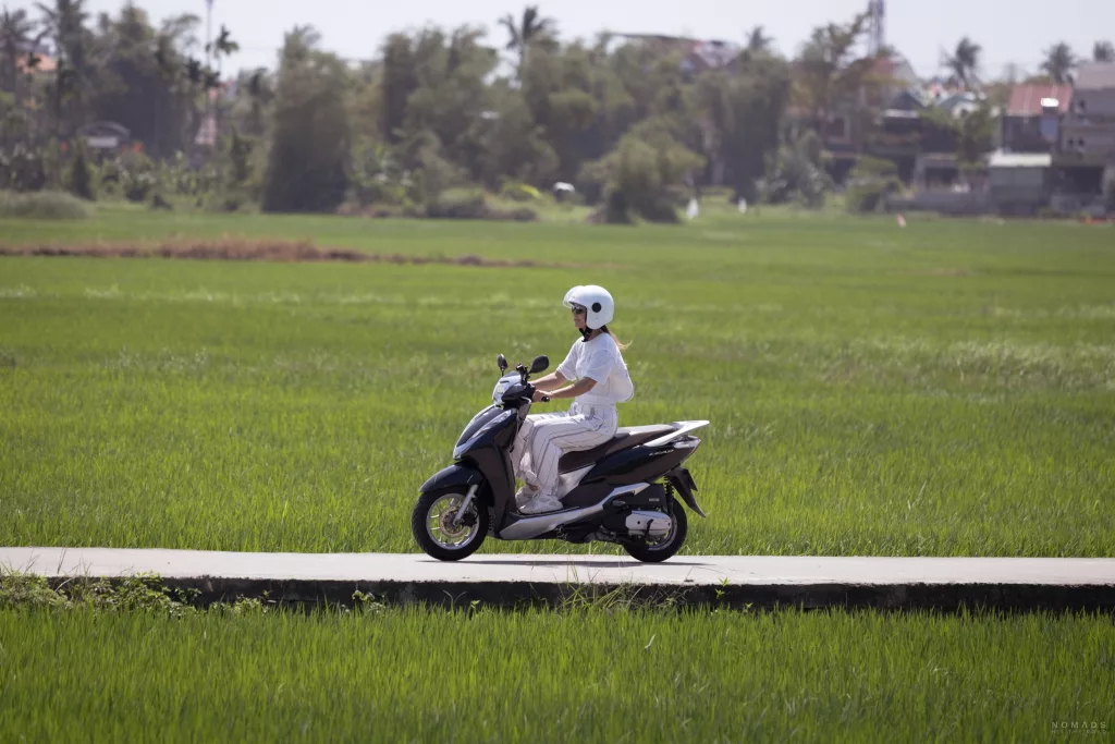 Frau fährt auf einem Roller auf einem Weg inmitten eines Reisfeldes in Hoi An