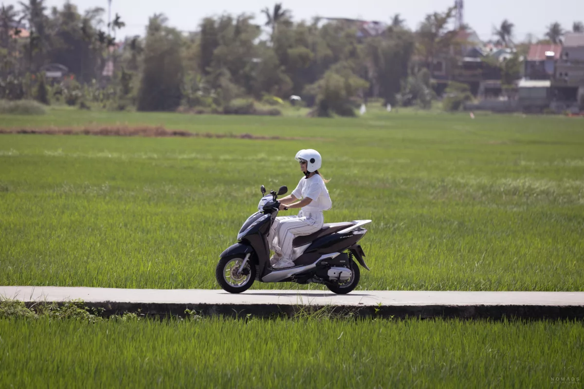 Frau fährt auf einem Roller auf einem Weg inmitten eines Reisfeldes in Hoi An