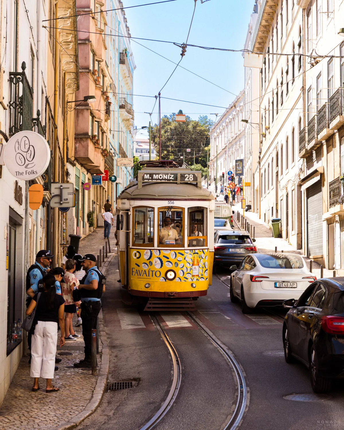 Gelbe Tram 28 fährt eine Straße hinunter, Menschen laufen auf dem Gehweg