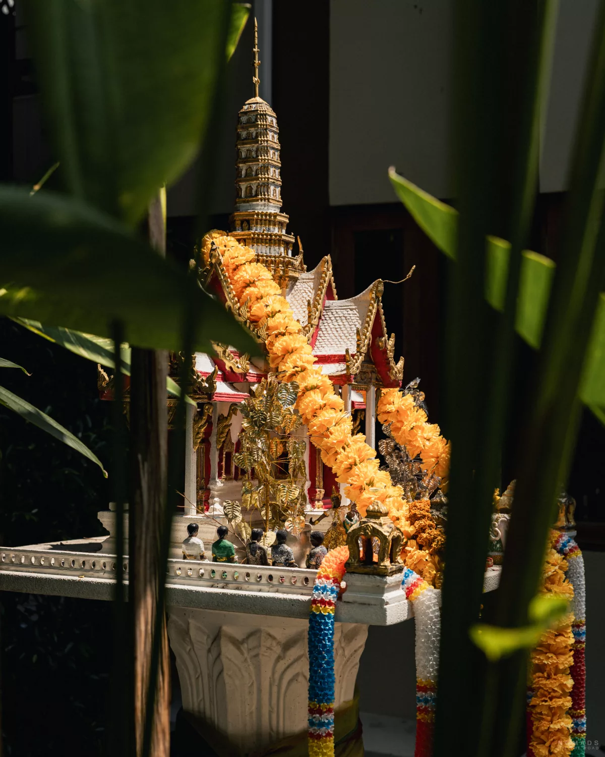 Buddhistischer Schrein behangen mit Blumenketten zwischen Pflanzen