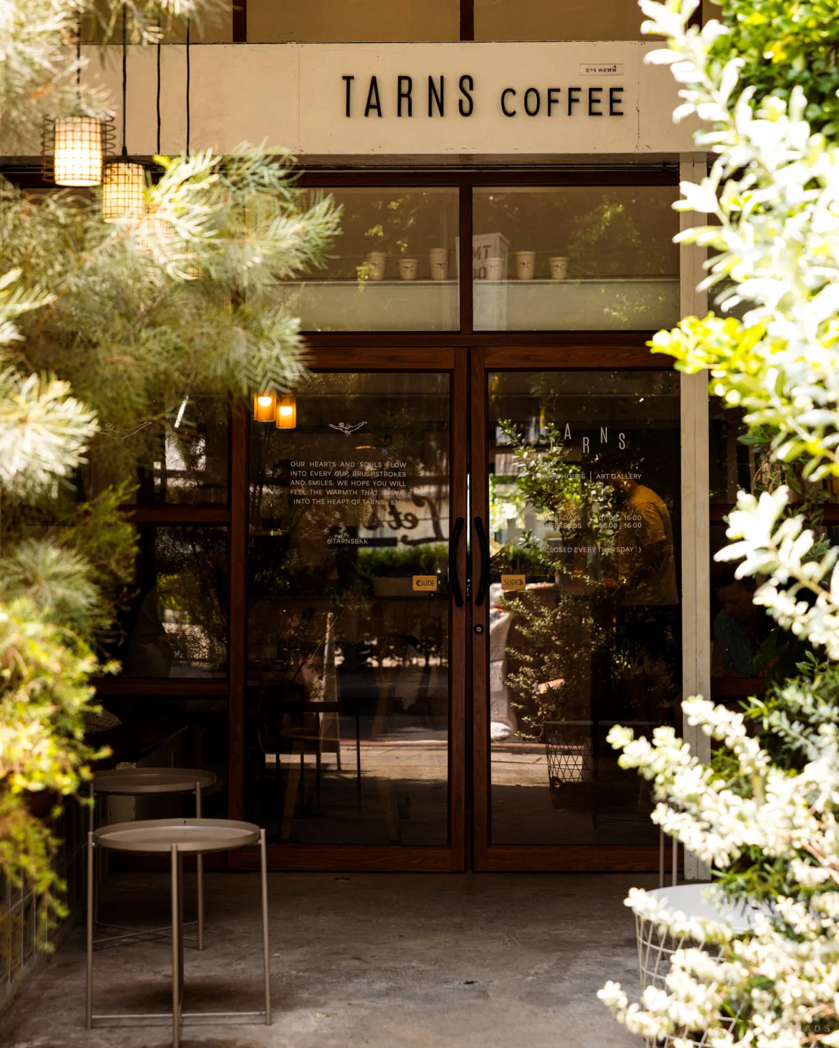 Eingang mit Pflanzen und kleinen Tischen vom Tarns Coffee in Bangkok