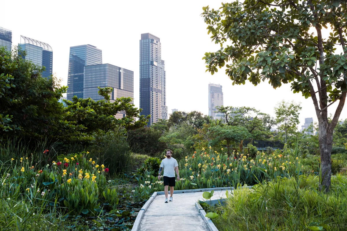 Mann läuft auf einem Weg zwischen Pflanzen, Bäumen und Blumen - im Hintergrund stehen Hochhäuser in Bangkok