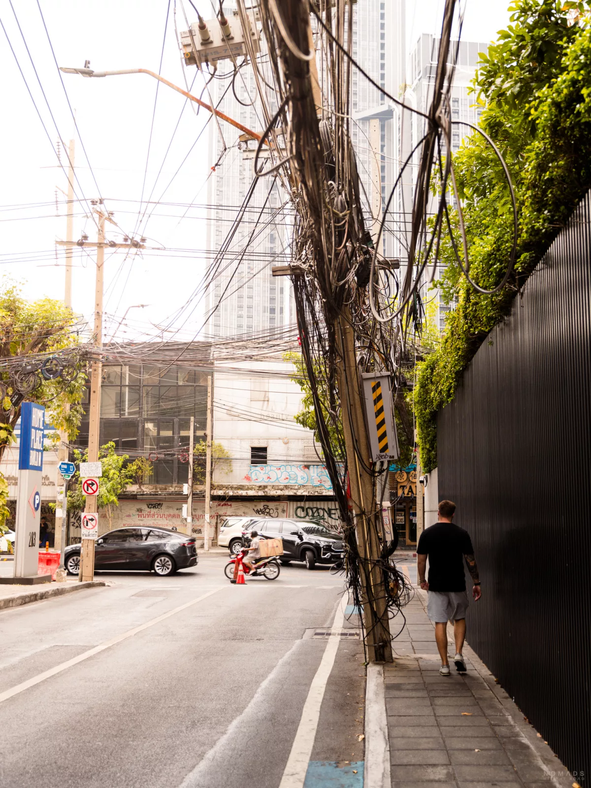 Mann läuft auf einem Bürgersteig in Bangkok neben ihm Mast mit unzähligen Kabeln