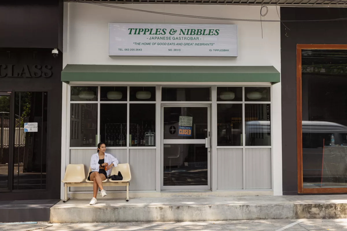 Frau sitzt vor dem Restaurant Tipples & Nibbles in Bangkok