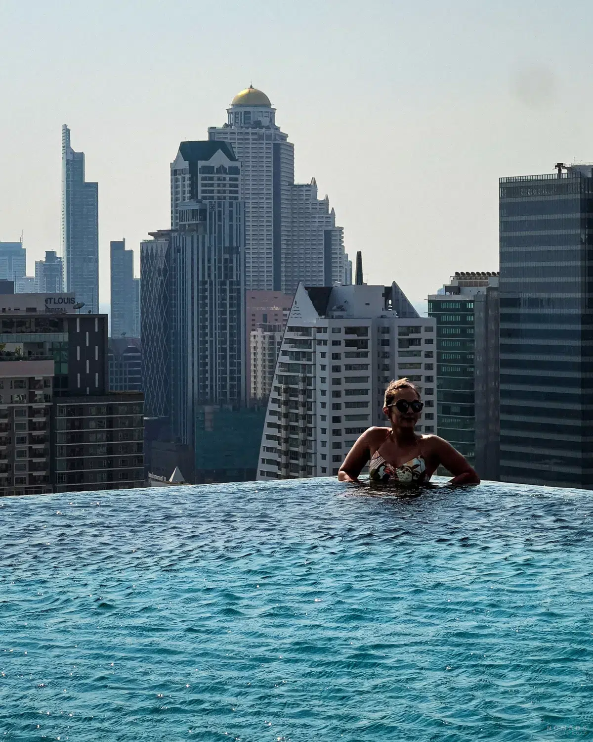 Frau sitzt in einem Pool über den Dächern in Bangkok mit Hochhäusern im Hintergrund im Stadtteil Sathorn