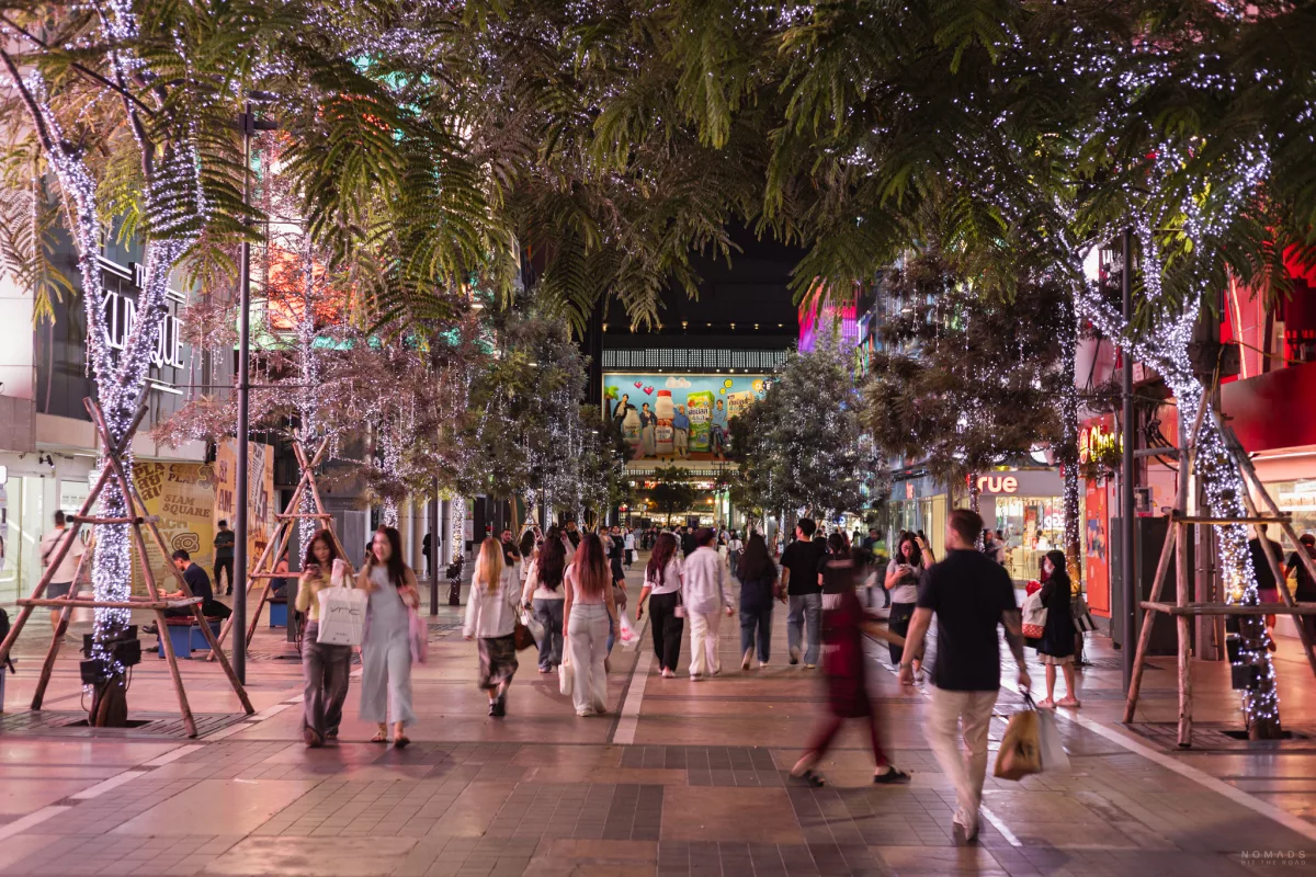 Menschen laufen am Siam Square entlang, wo beleuchtete Bäume stehen