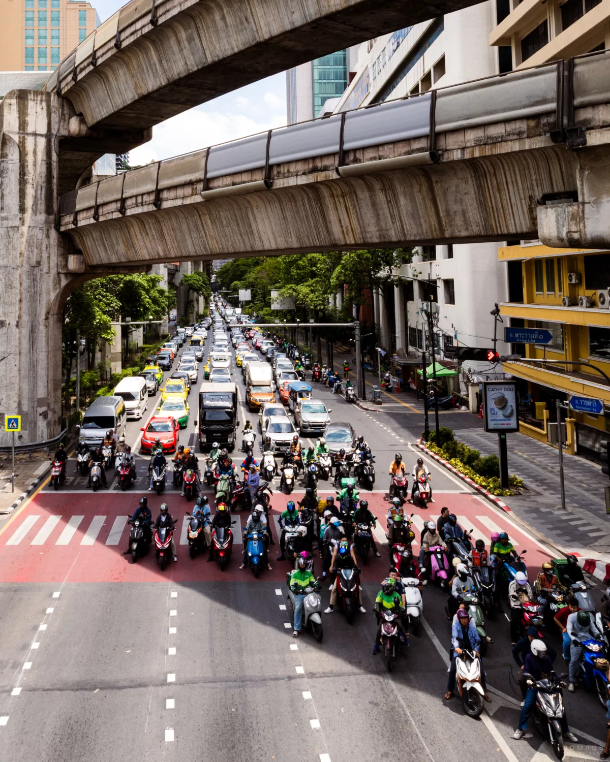 Autos und Rollerfahrer stehen an einer roten Ampel in Bangkok unter einer Bahnüberführung