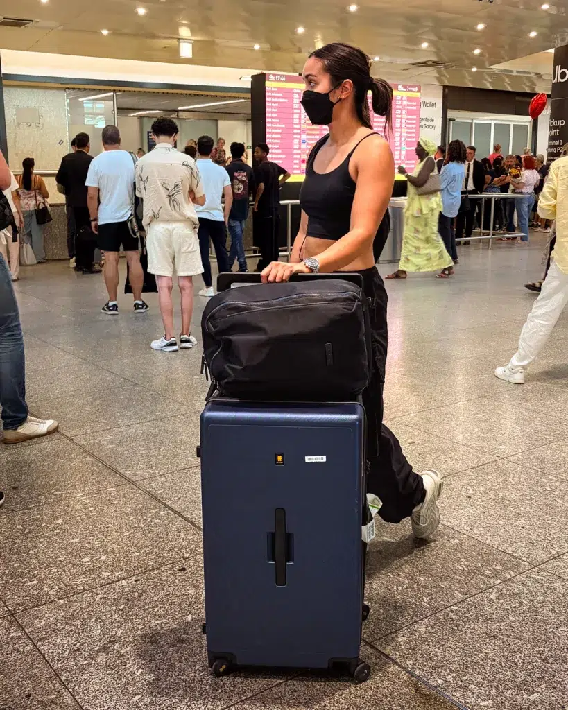 Frau schiebt ihren Koffer mit aufgelegten Rucksack durch einen Flughafen