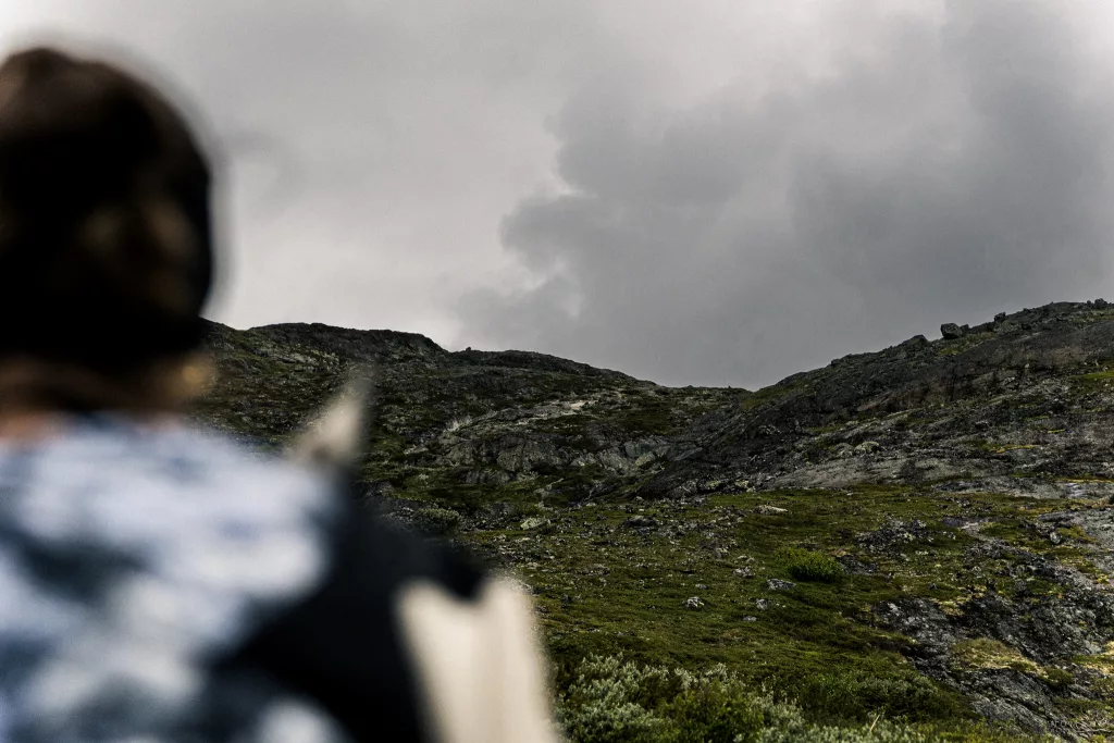 Blick über die Schulter einer Person mit Blick auf den Berg auf der Besseggen Wanderung in Norwegen, über dem eine Wolke hinwegzieht