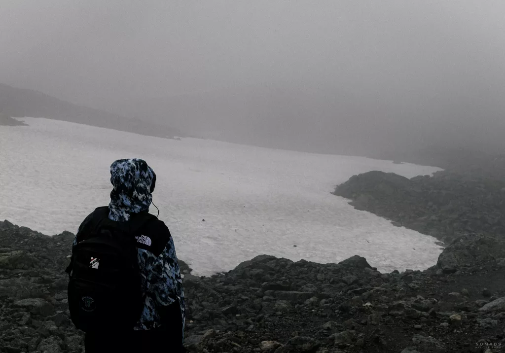 Frau in Regenjacke steht vor einer Schneefläche während der Besseggen Wanderung in Norwegen