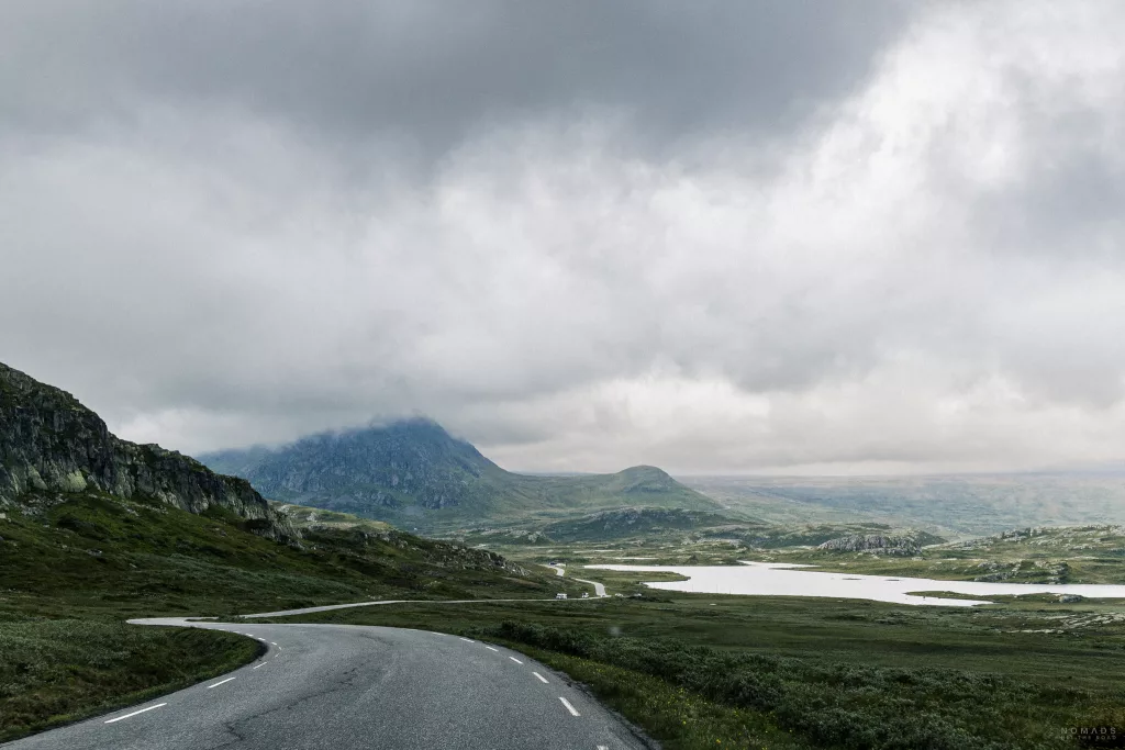 Blick auf die Passstraße Valdresflye umgeben von grünen Flächen, Bergen und einer Wolkenfront am Himmel