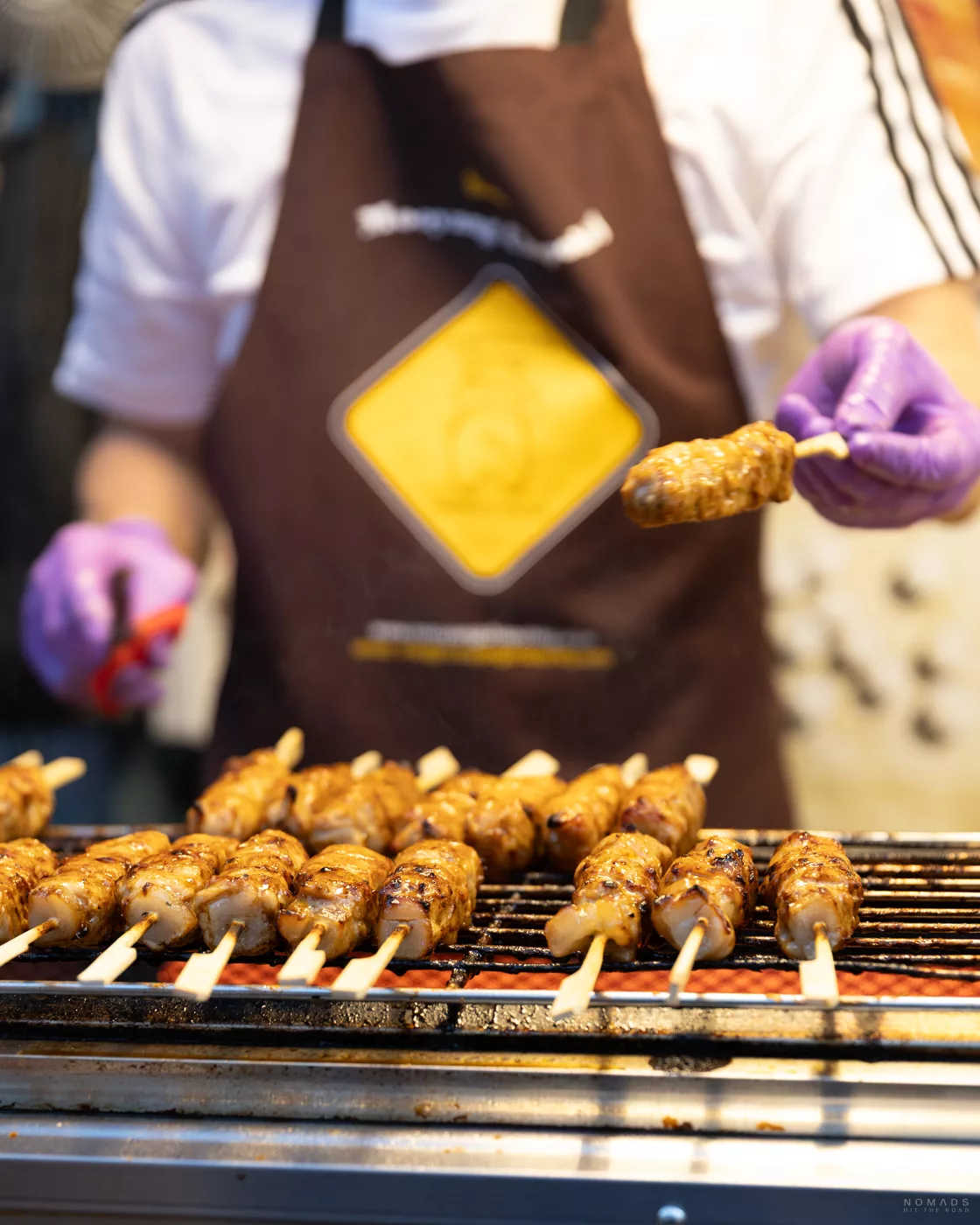 Mann mit lila Handschuh überreicht einen Spieß mit Fleisch vom Grill