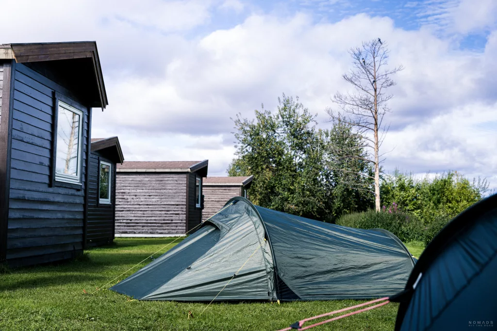 Zelte auf einer Wiese hinter Holzhütten auf dem Alta Strand Camping & Apartment
