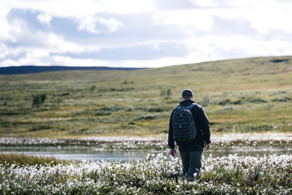 Mann mit Rucksack läuft über eine Wiese mit weißen Blumen