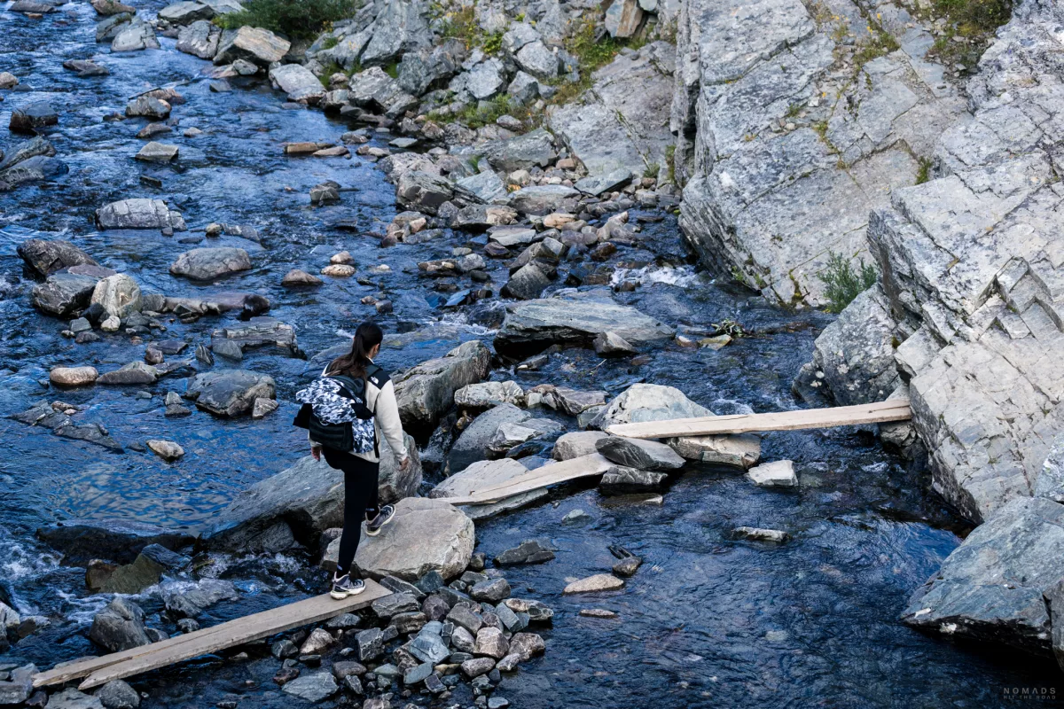 Frau mit Rucksack überquert einen Fluss über Holzplanken