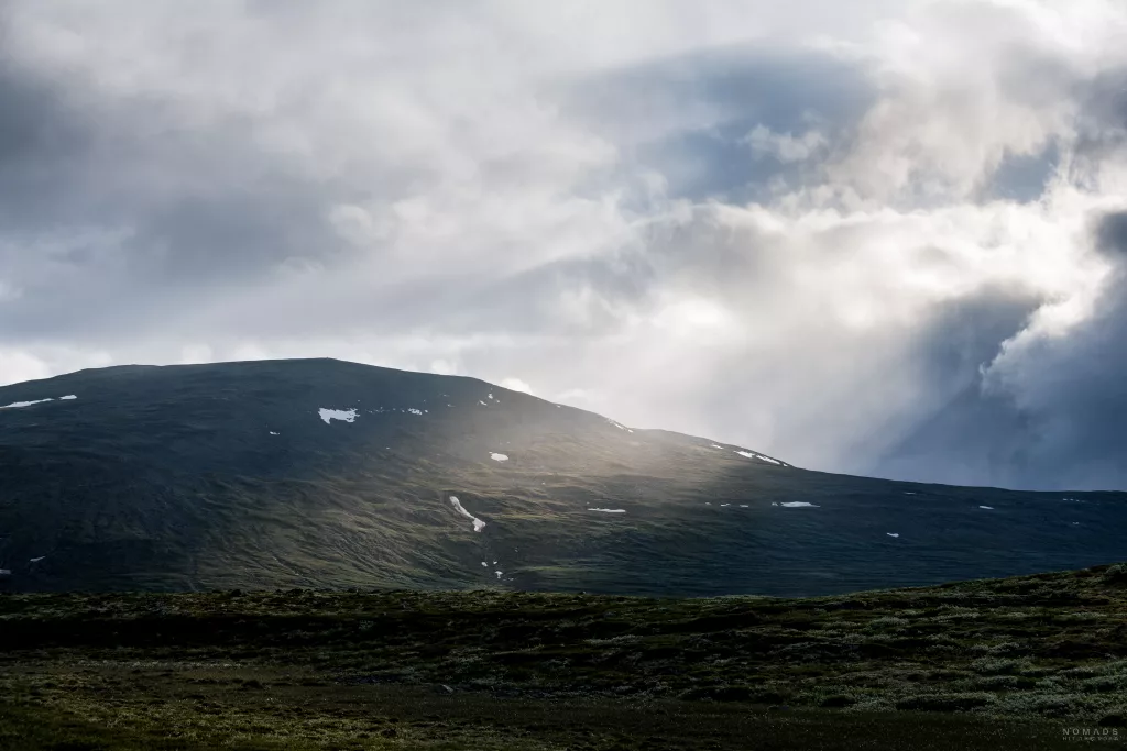 Sonnenstrahlen scheinen durch dichte Wolken auf die Hochebene im Dovrefjell Nationalpark