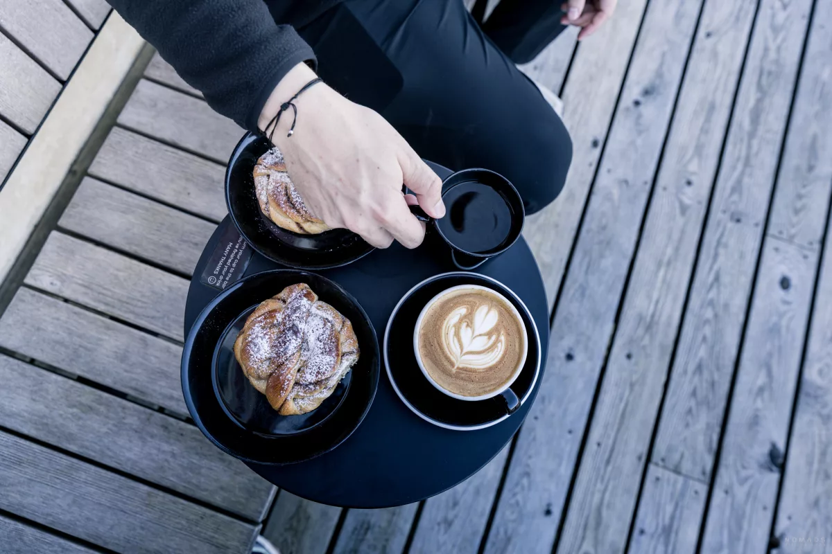 Tisch auf dem Gebäck und Kaffee steht, Person greift nach einer Tasse