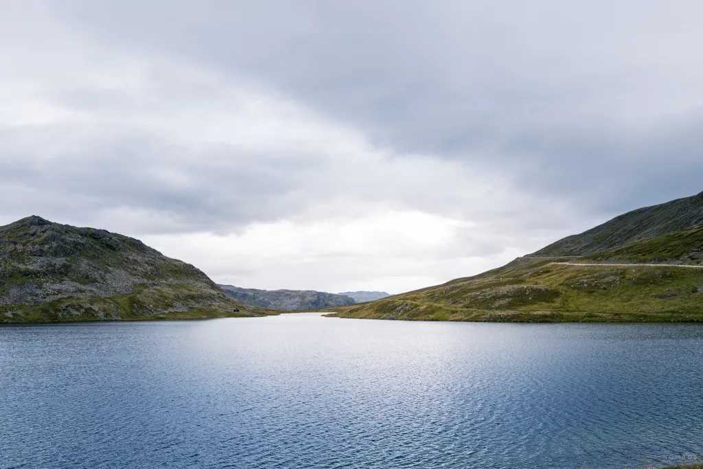 Blick auf eine Passstraße sowie See umgeben von grün bewachsenen Hügeln