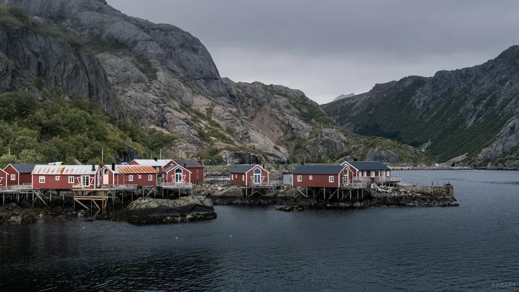 Rote Fischerhäuser am Wasser mit Bergen im Hintergrund