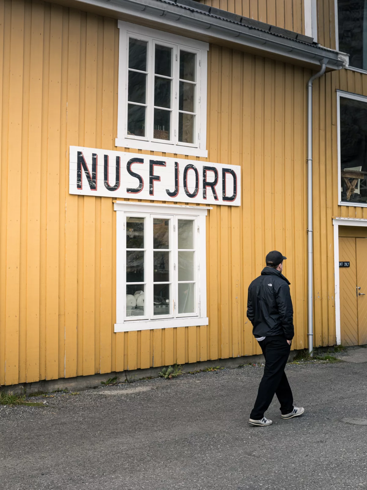 Mann läuft an einem gelben Gebäude vorbei an dem Nusfjord steht