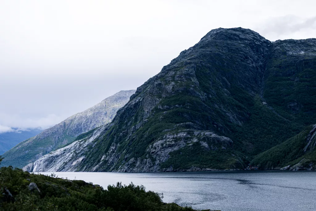 Blick auf einen grün bewachsenden Berg, der im Fjord liegt