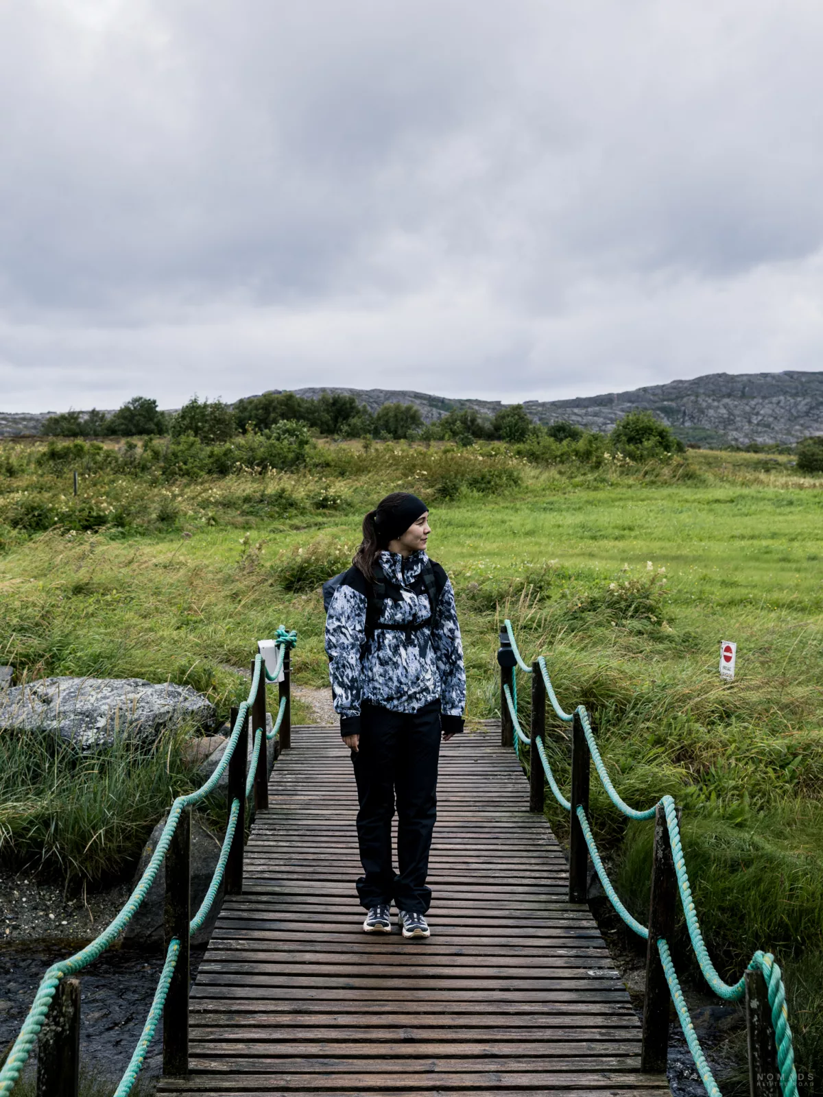 Frau steht auf einer Holzbrücke am Torghatten, im Hintergrund Wiese und Büsche