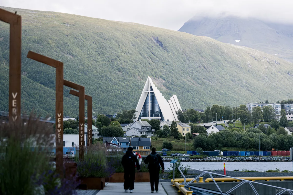 Zwei Menschen laufen auf einer Promenade in Tromsø, im Hintergrund steht die Eismeerkathedrale