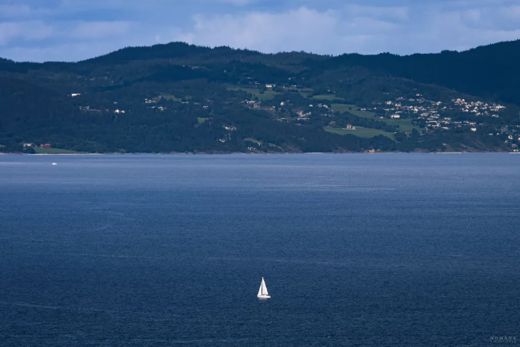 Segelboot schippert über den Trondheimer Fjord, im Hintergrund Berge, Häuser und viel Grün
