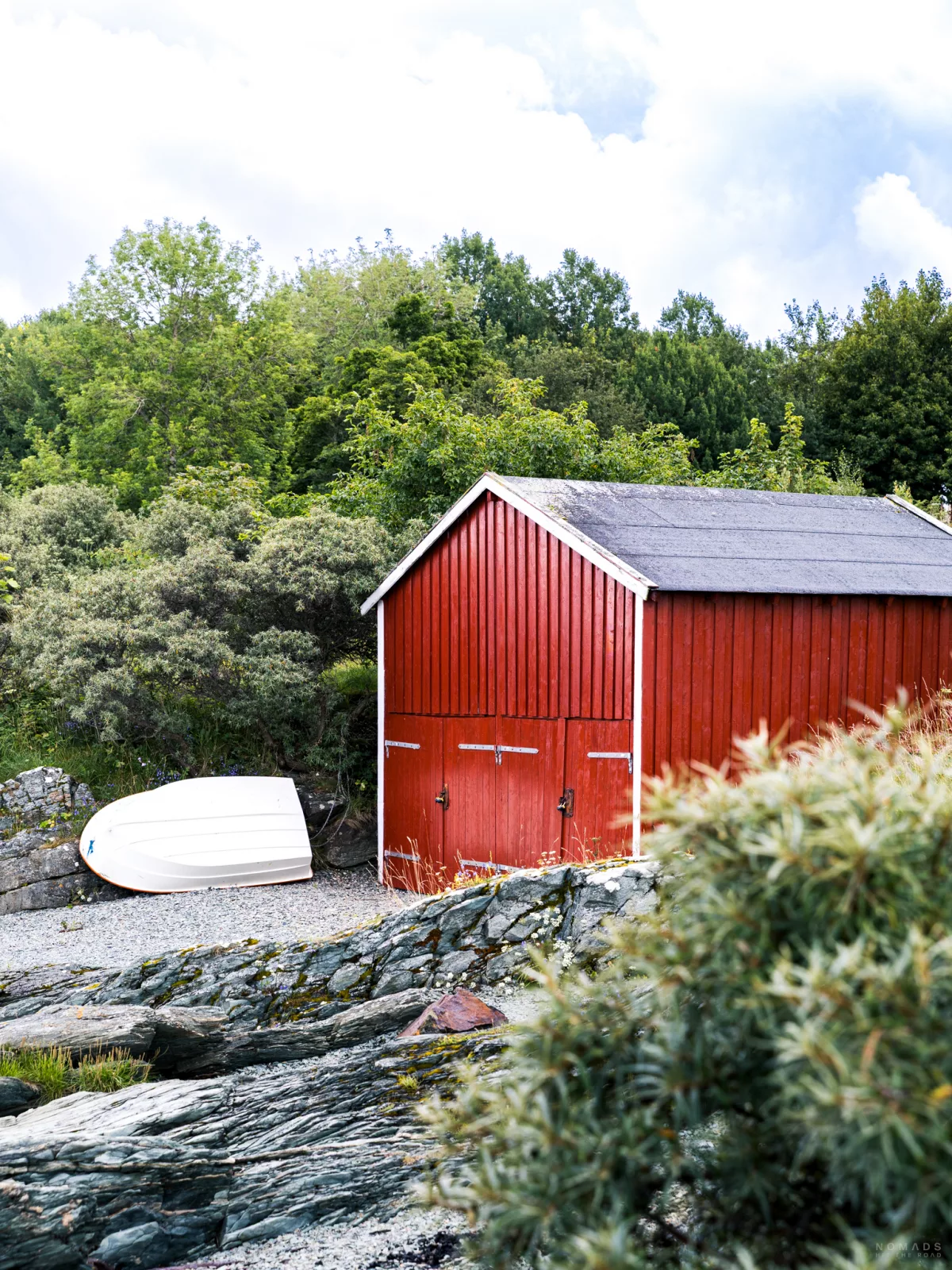 Rotes Bootshaus am Strand, daneben ein weißes kleines Boot