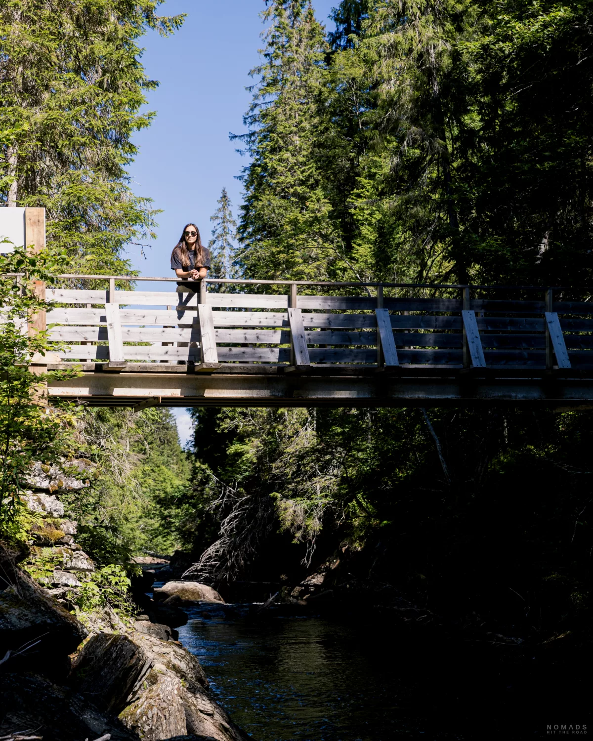 Frau steht auf einer Holzbrücke, die über einen Fluss im Wald führt