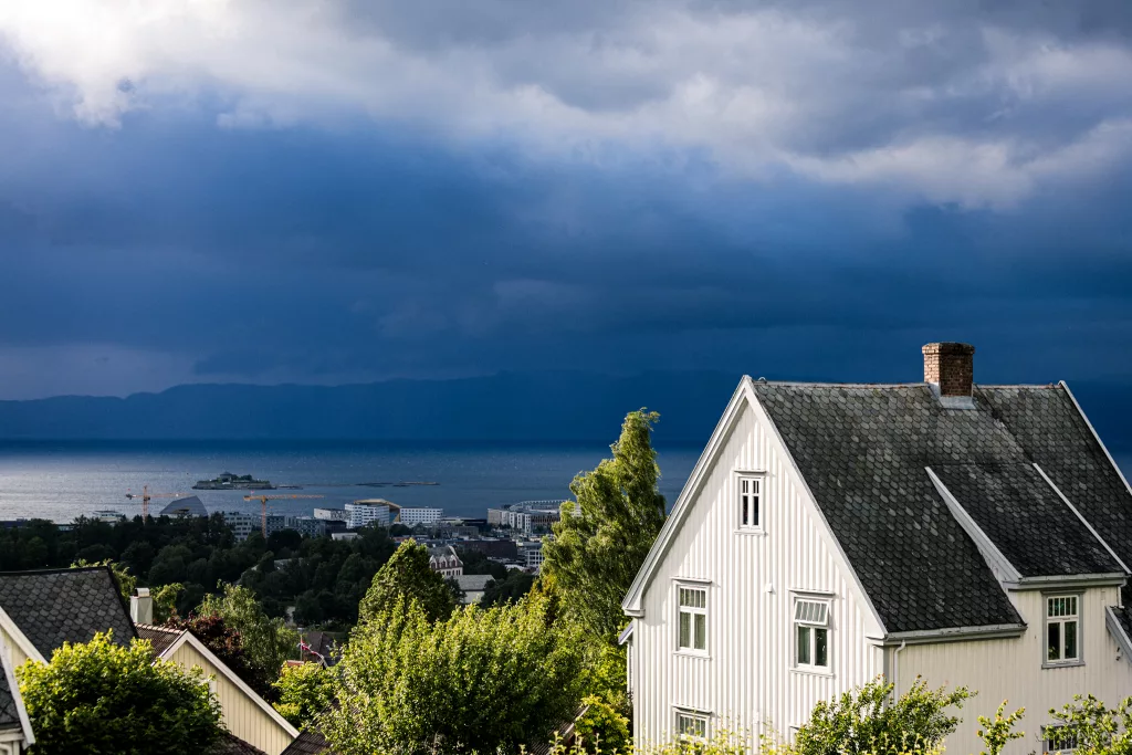 Blick an einem weißen Haus vorbei auf die dunkle Regenwolke, die über dem Trondheimer Fjord aufzieht