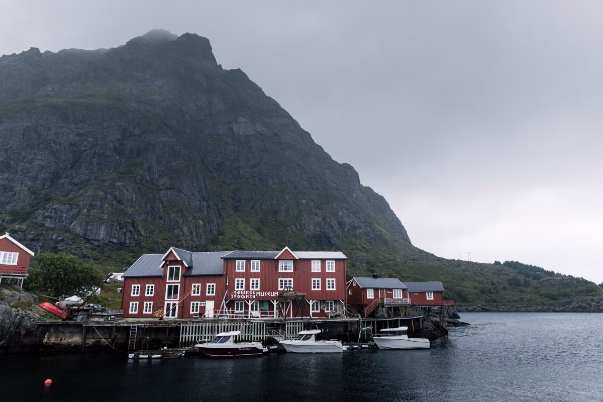 Rote Rorbuer in Å i Lofoten vor vernebelten Bergen und Booten davor