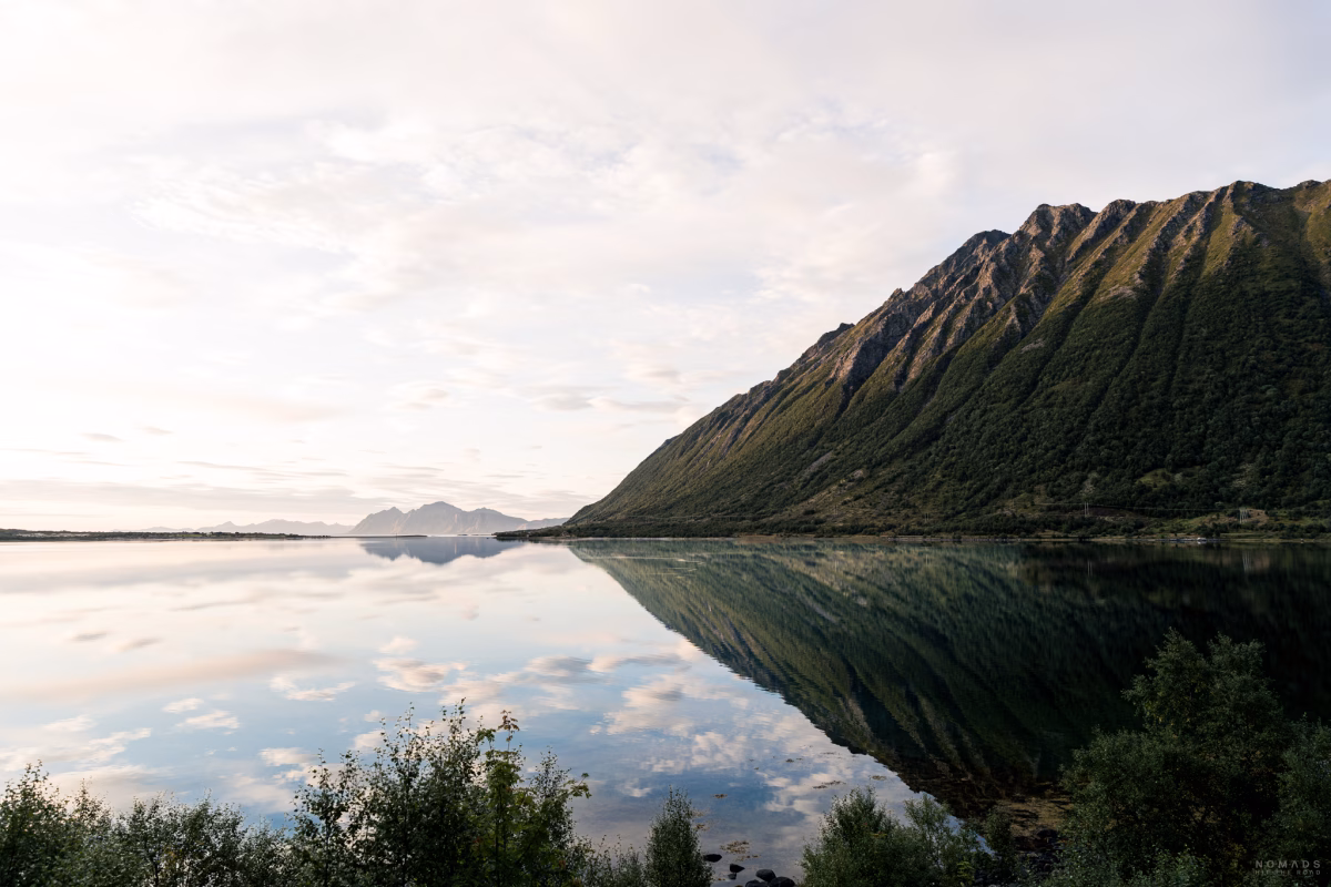 Blick auf einen grün bewachsenen Berg auf Andøya, der sich im Wasser spiegelt
