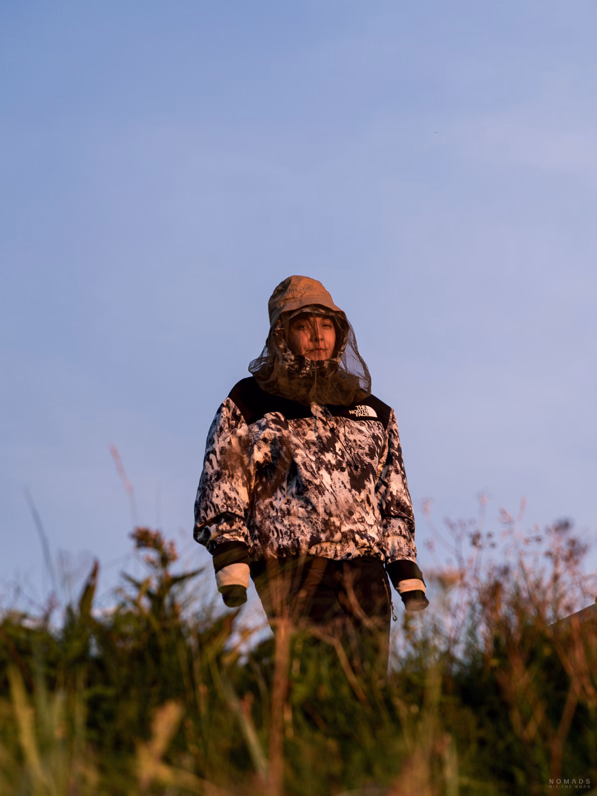 Frau steht mit Regenjacke und Netzhut am auf einer Wiese