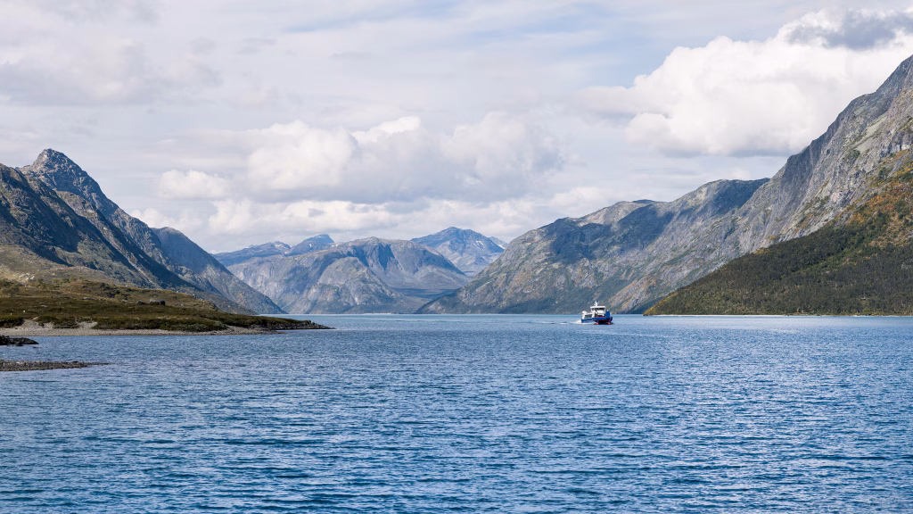 Blick auf den See Gjende mit umliegenden Gebirgsketten und einer Fähre auf dem Wasser