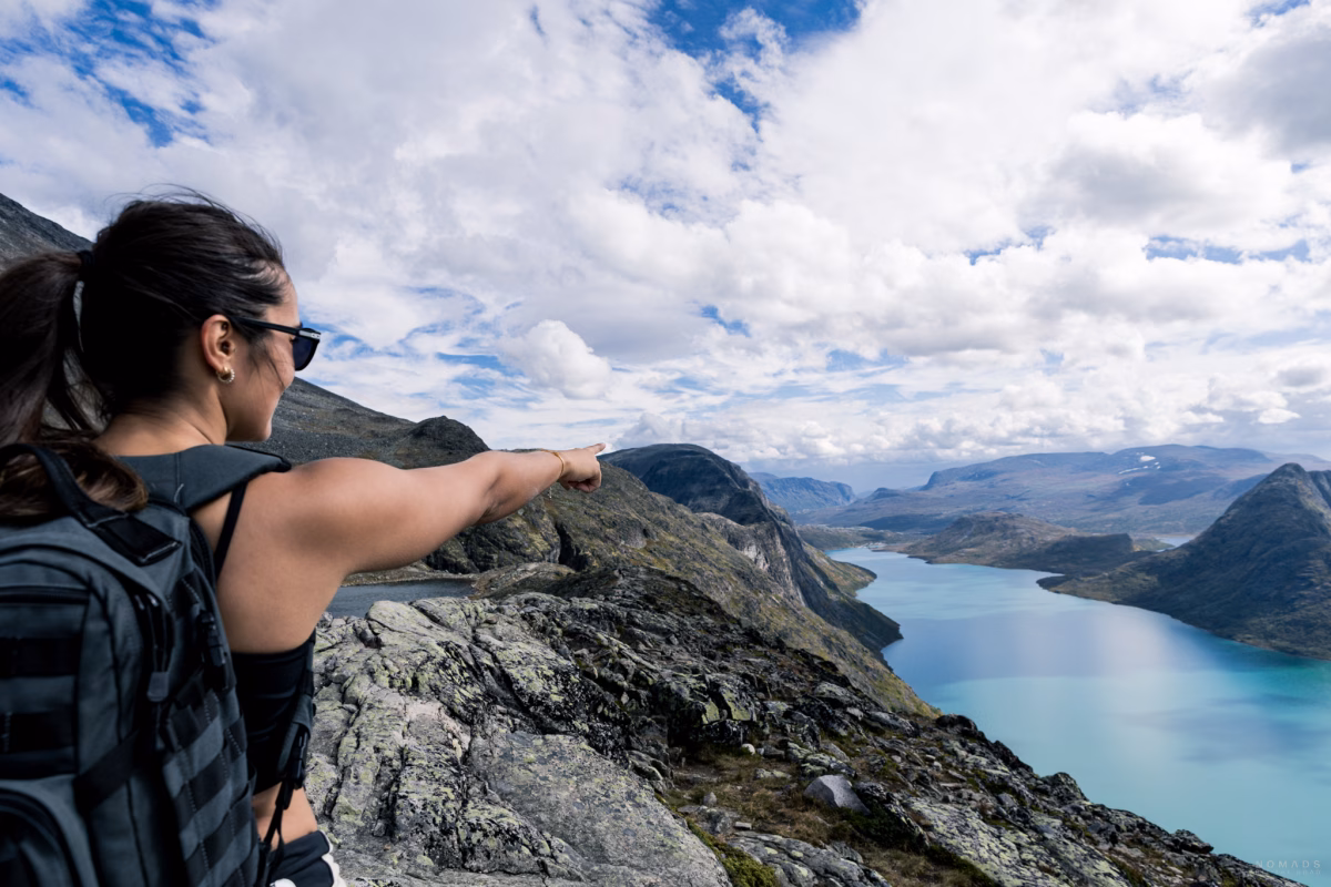 Frau zeigt auf den Berggipfel des Besseggen, unten im Tal blaues Wasser im See