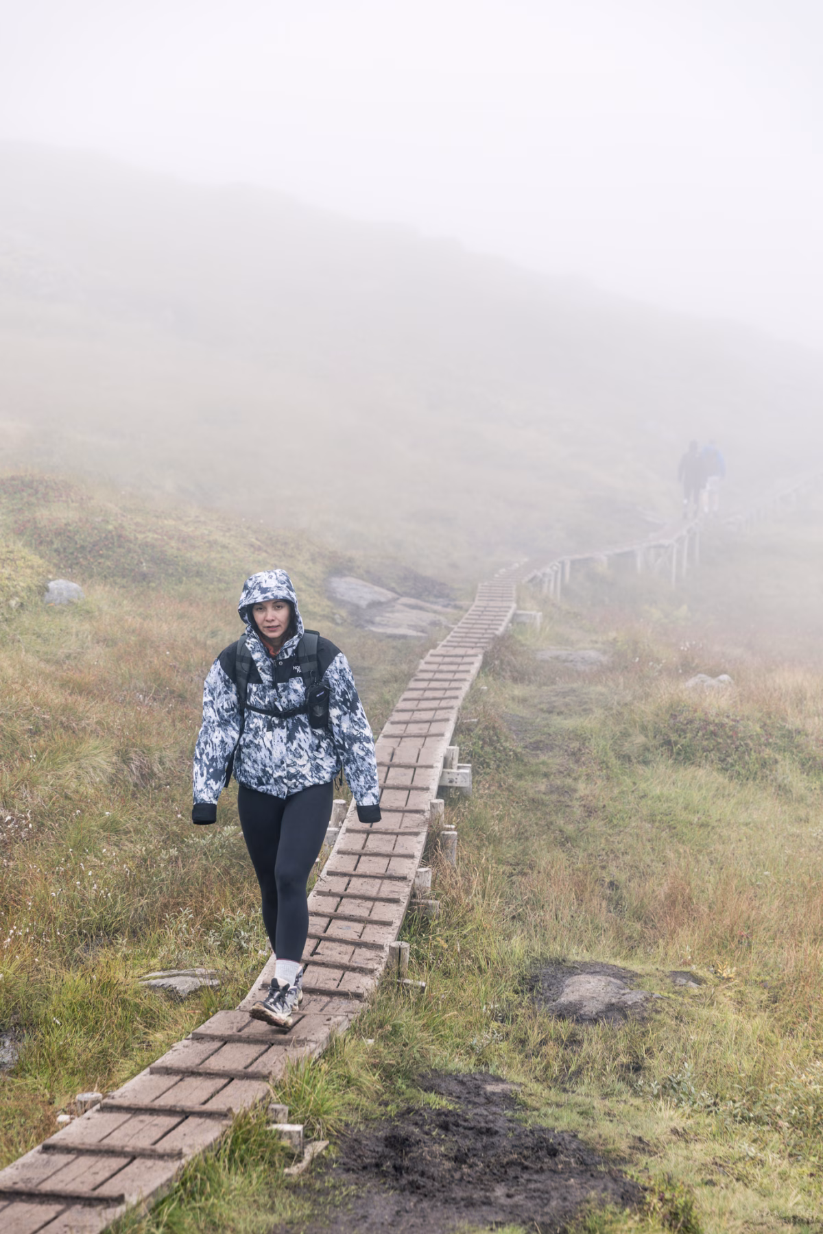 Frau läuft bei Nebel auf Holzbohlen auf einem Wanderweg zum Ryten