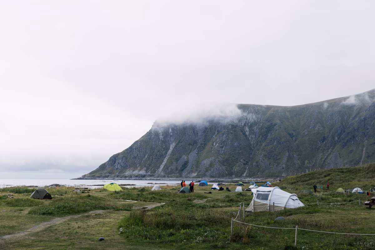 Blick auf den Zelte auf der Wiese auf dem Lofoten Beach Camp, das am Strand liegt und im Hintergrund auf Berge blickt