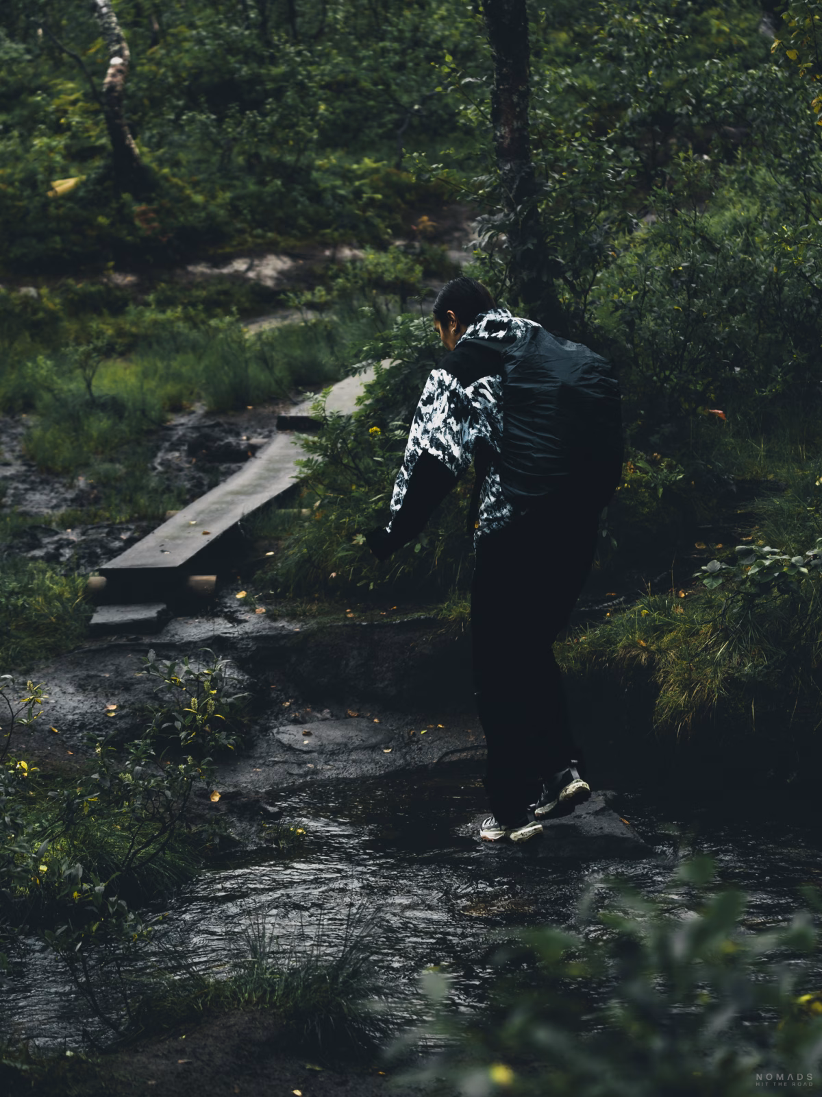 Frau läuft im Regen über einen Bachlauf im Wald