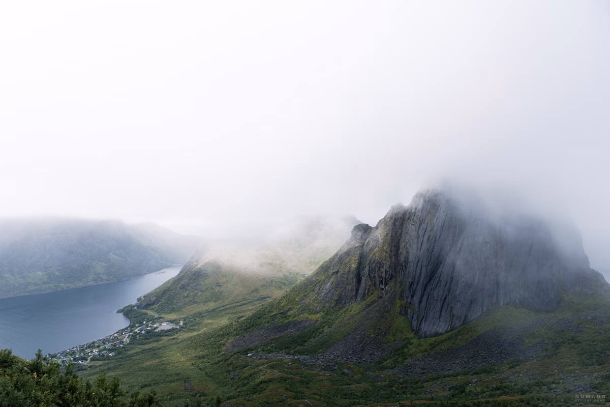Blick auf den vernebelten Berg Segla mit Dorf unten am Fjord