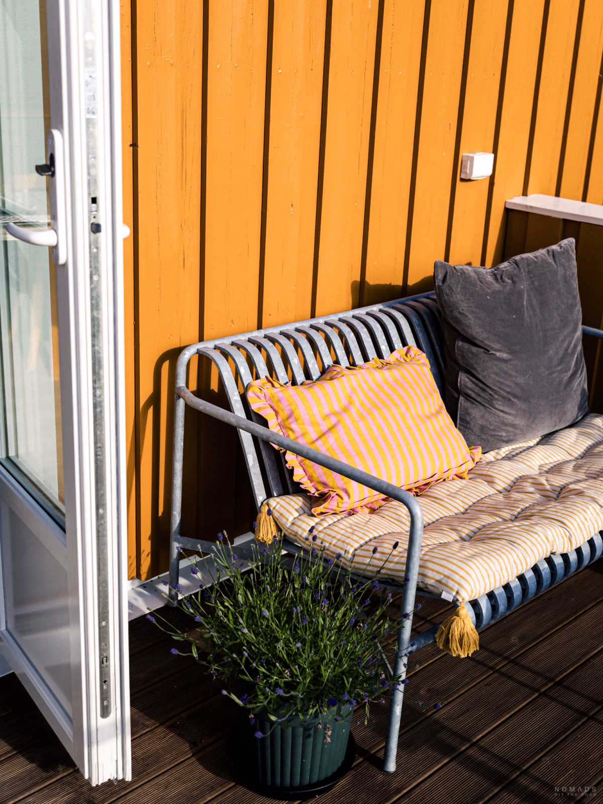 Sitzbank mit Kissen steht auf einem Balkon mit gelber Holzfassade